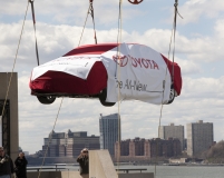 A crane lifts a mystery Toyota model to the top level of the Javits Convention Center,